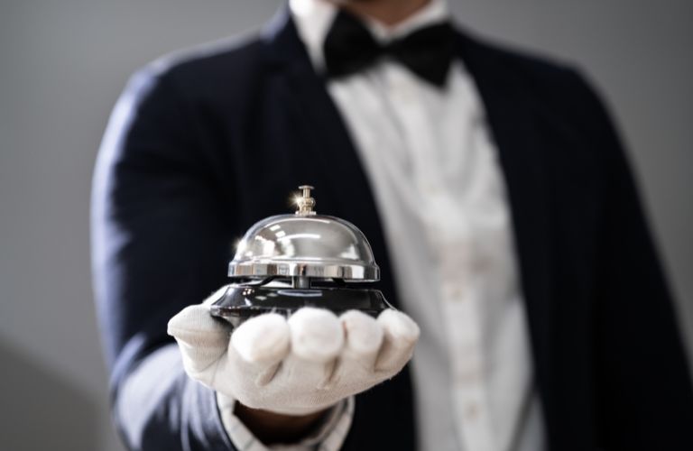 Butler or Bellhop in Black Tuxedo Holding Silver Bell in Gloved Hand