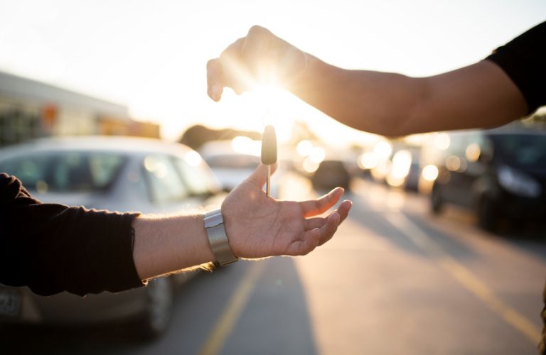 Dealer Handing Keys of a New Car to Car Shopper with Sun in the Background