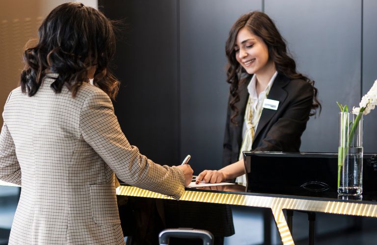 Woman Helping a Woman at Hotel Reception Desk