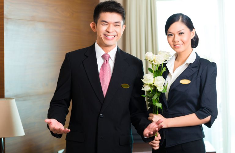 Smiling Man and Woman Hotel Workers Holding White Flowers