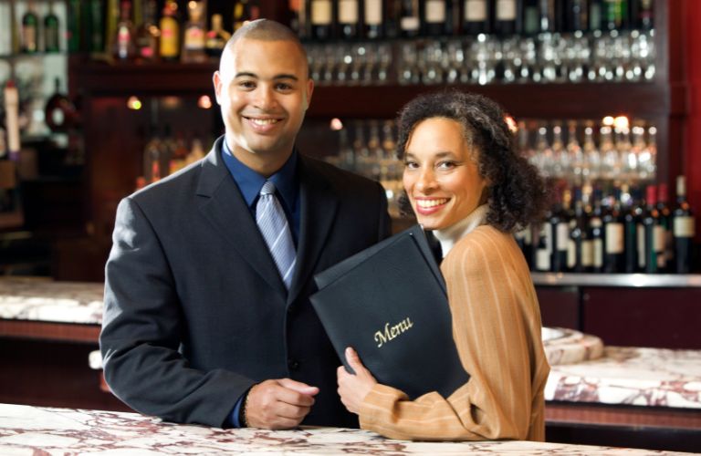 Smiling Man and Woman in a Restaurant by the Bar Holding a Menu