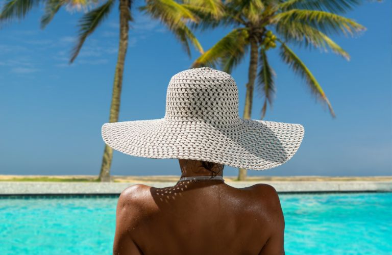 Woman in a White Sunhat Sitting by a Pool and Beach